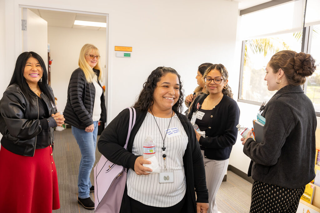A group of women smiling and chatting during a San Pedro clinic tour, fostering connections and collaboration in a bright and welcoming space.